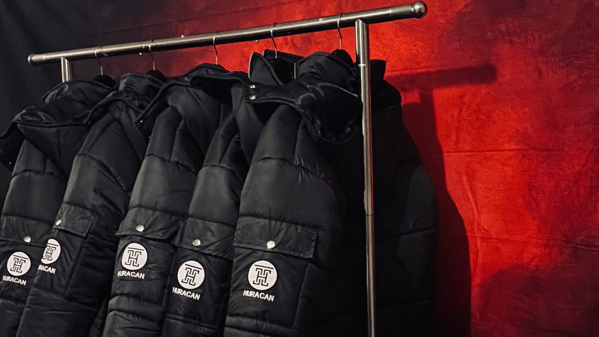 The Signature Huracan Men &amp; Women's Black Puffer Jacket hooded on railings