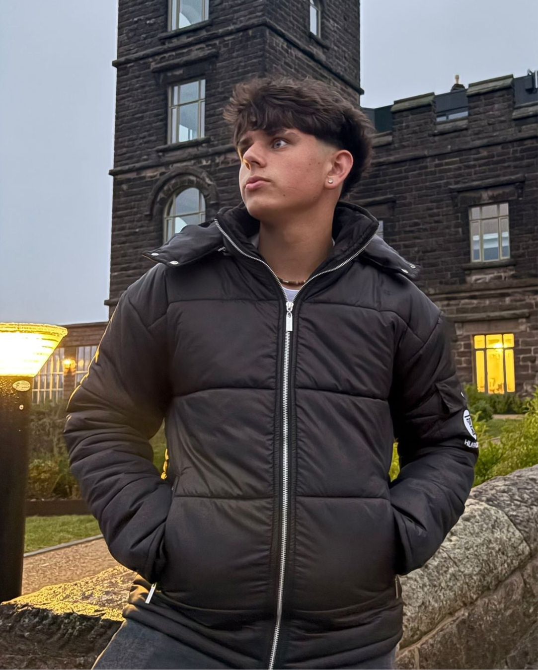 The Signature Huracan Men &amp; Women's Black Puffer Jacket hooded standing in front of castle front side