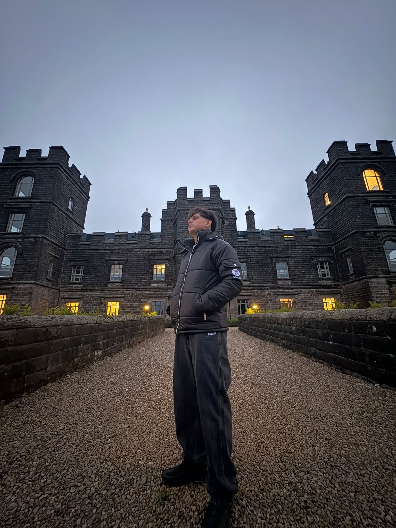 The Signature Huracan Men &amp; Women's Black Puffer Jacket hooded standing in front of castle front side angle